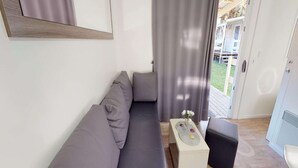 Un soggiorno moderno con un divano grigio, un piccolo tavolino bianco con un vaso e un pouf nero.