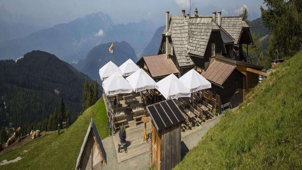 A mountain lodge with wooden cabins, outdoor seating, and a view of the surrounding mountains.