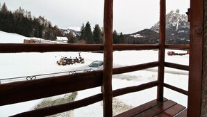 Un balcón de madera con vistas a un paisaje nevado, que incluye una montaña y un coche estacionado.