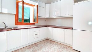 Eine Küche mit weißen Schränken, einem Fenster mit Holzrahmen und einem Kühlschrank.