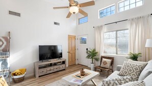 A spacious living room with a ceiling fan, a flat-screen TV, a wooden coffee table, and a sofa. - 2BR Serene Red Rock Retreat - Hot Tub & Nice Views (Sedona)
