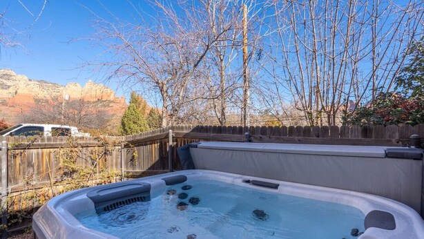 A hot tub in a backyard with a wooden fence, trees, and a mountainous backdrop. - 2BR Serene Red Rock Retreat - Hot Tub & Nice Views (Sedona)