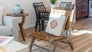 A wooden chair with a woven seat and a decorative pillow, placed in a room with a dining table and chairs, a small side table, and a potted plant. - 2BR Serene Red Rock Retreat - Hot Tub & Nice Views (Sedona)