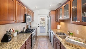 A kitchen with wooden cabinets, granite countertops, stainless steel appliances, and a view through a glass door. - 2BR Serene Red Rock Retreat - Hot Tub & Nice Views (Sedona)