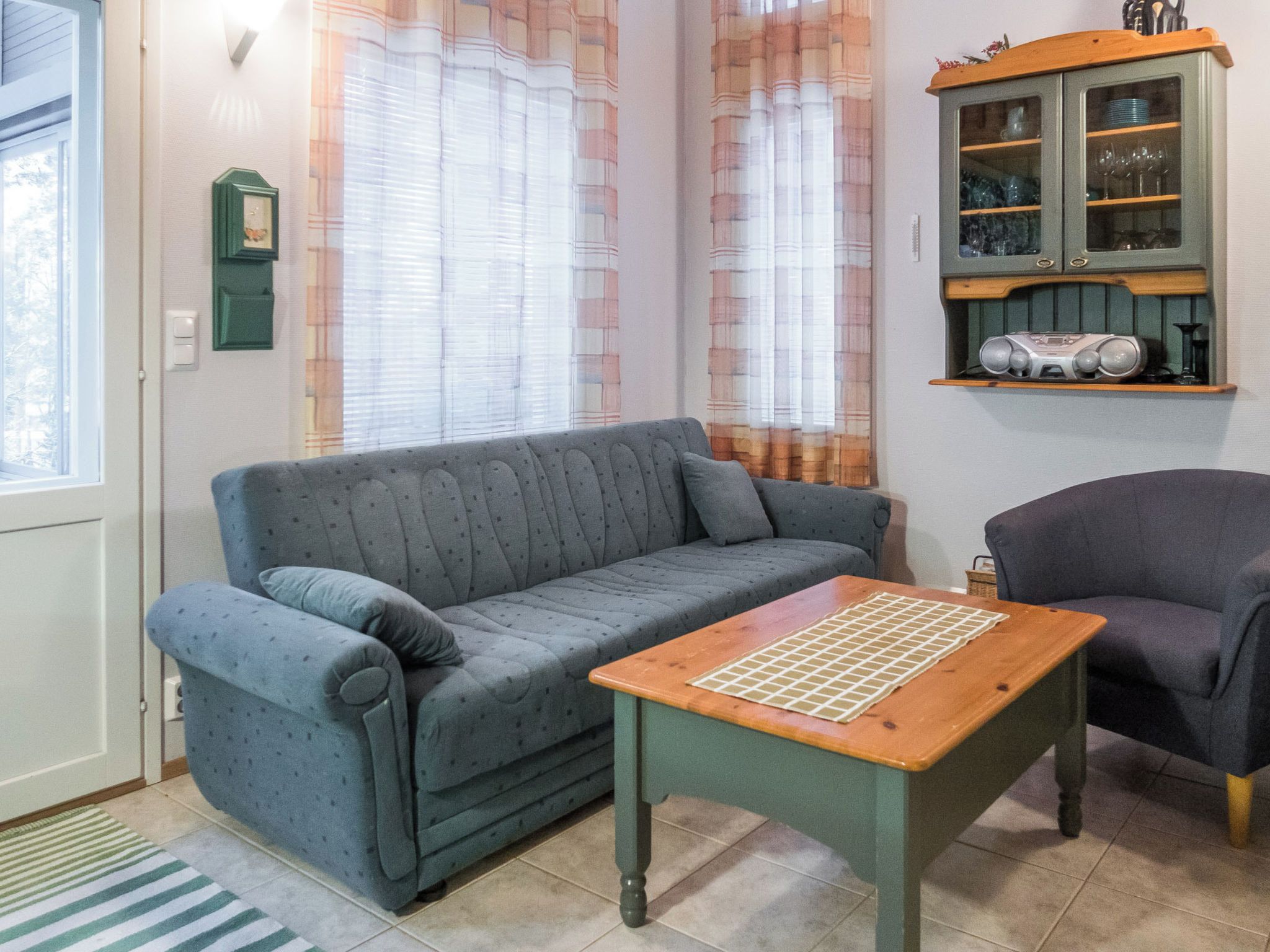 Una habitación con un sofá gris, una mesa de madera con diseño de cuadrícula, un sillón oscuro y un armario con puertas de cristal.