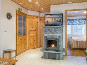 Una habitación con chimenea de piedra, puertas de madera, un televisor sobre un mueble y una cama con colcha estampada.