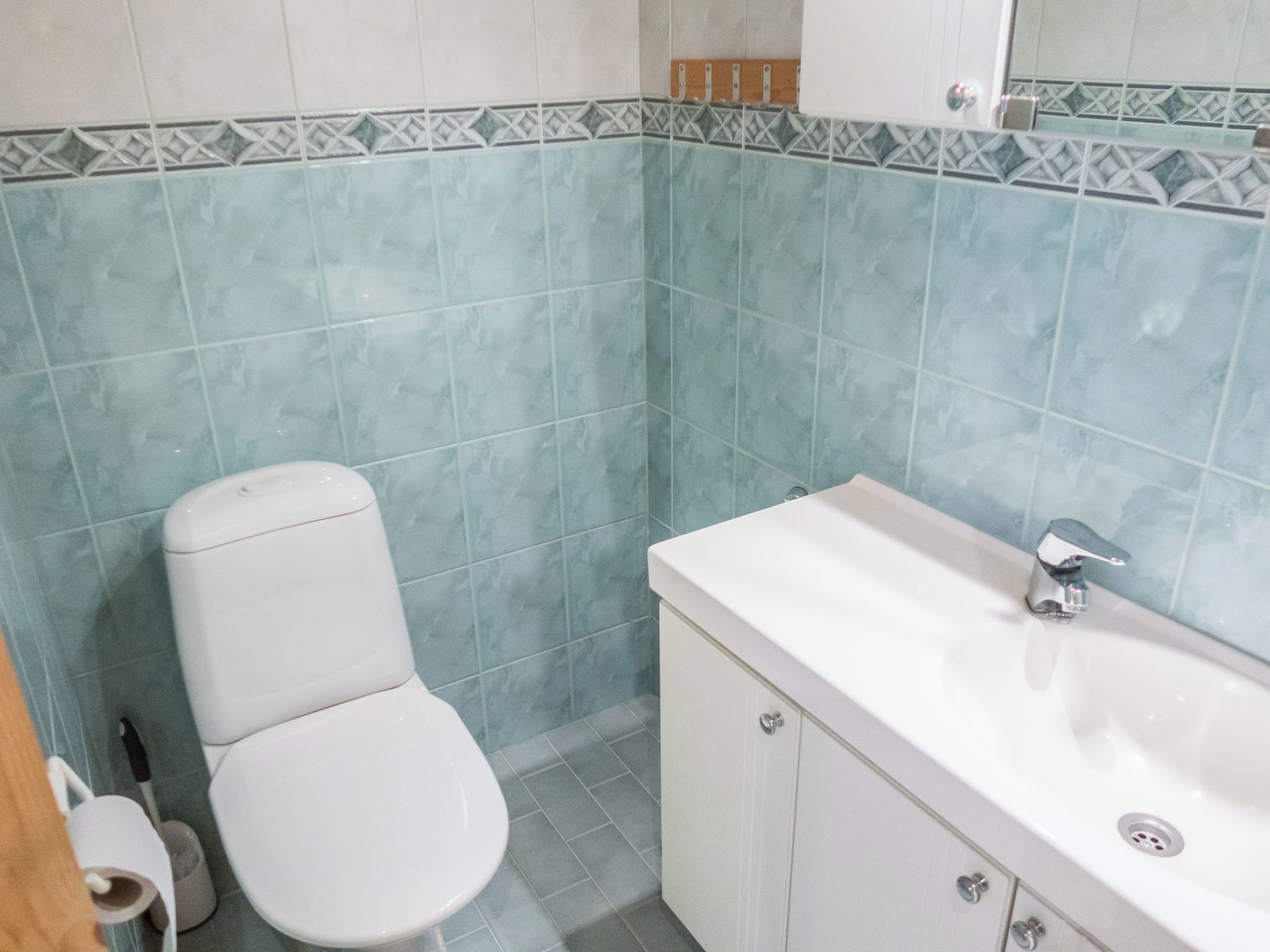 Casa de banho com sanita, lavatório e paredes revestidas a azulejos.