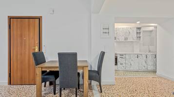 Un comedor con una mesa de madera y cuatro sillas, una cocina con muebles blancos de mármol y un suelo de terrazo.