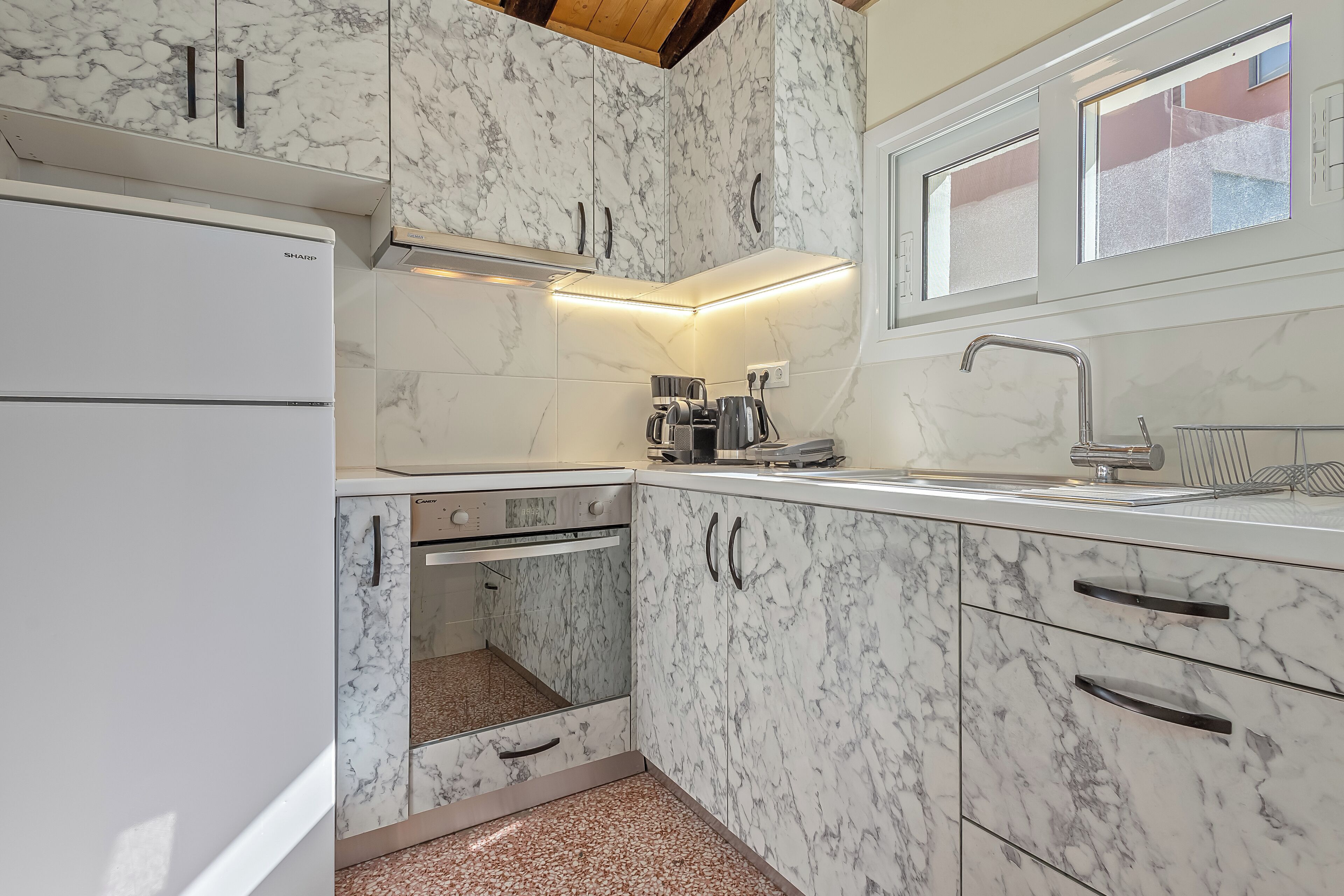 Una cocina compacta con horno empotrado, cafetera y ventana sobre el fregadero.
