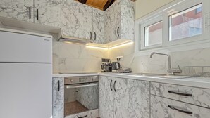 A compact kitchen with a built-in oven, a coffee machine, and a window above the sink. - Athens Plaka Family Suites (Athens)