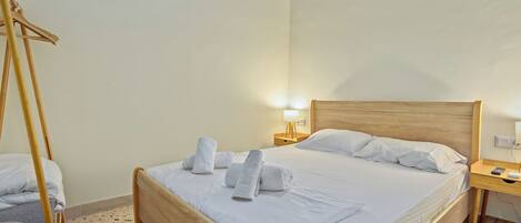A hotel room with a wooden bed, white linens, a wooden nightstand with a lamp, and a wooden chair.