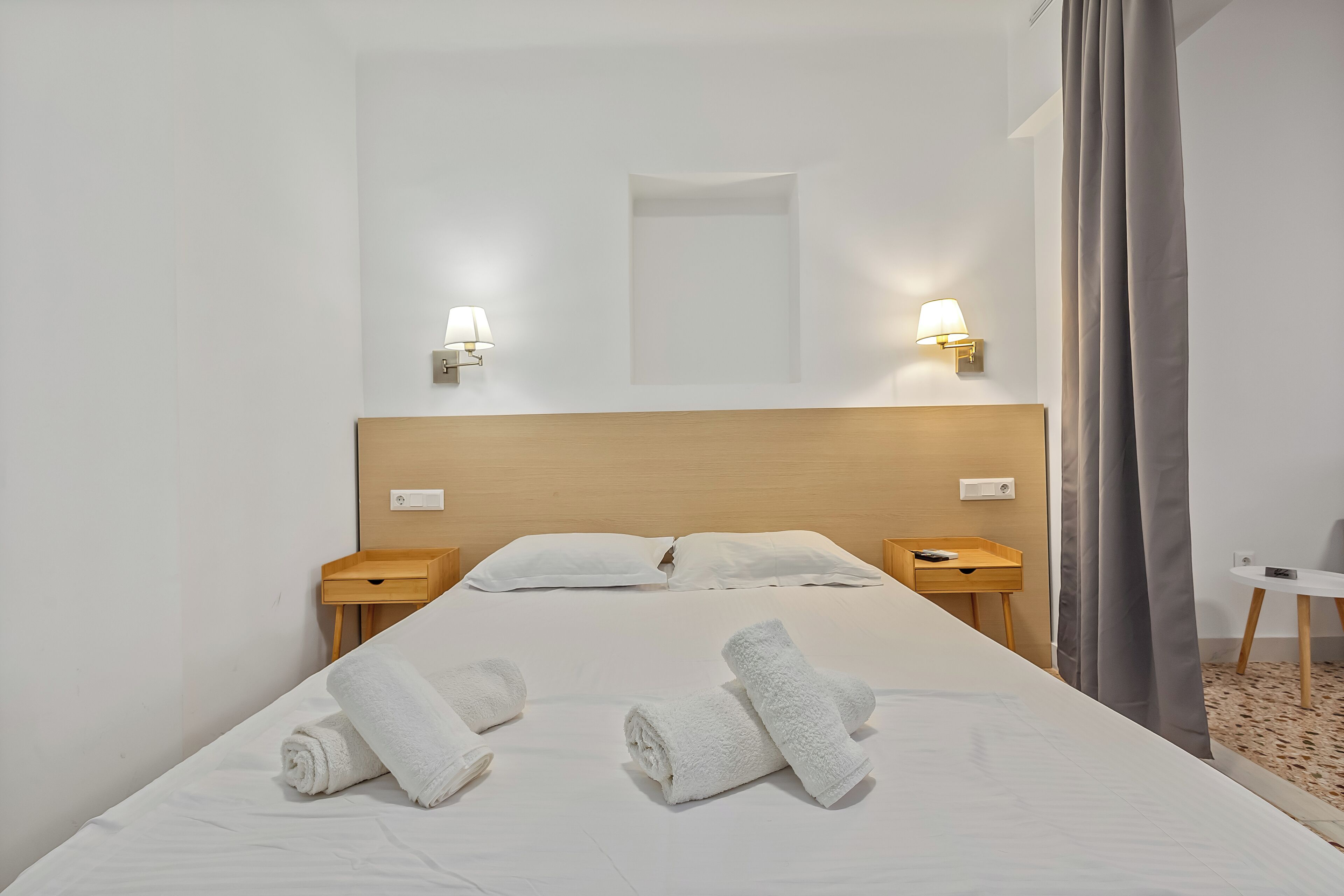 A hotel room with a large bed, two bedside tables, a nightstand, a wall-mounted lamp, and a small round table.