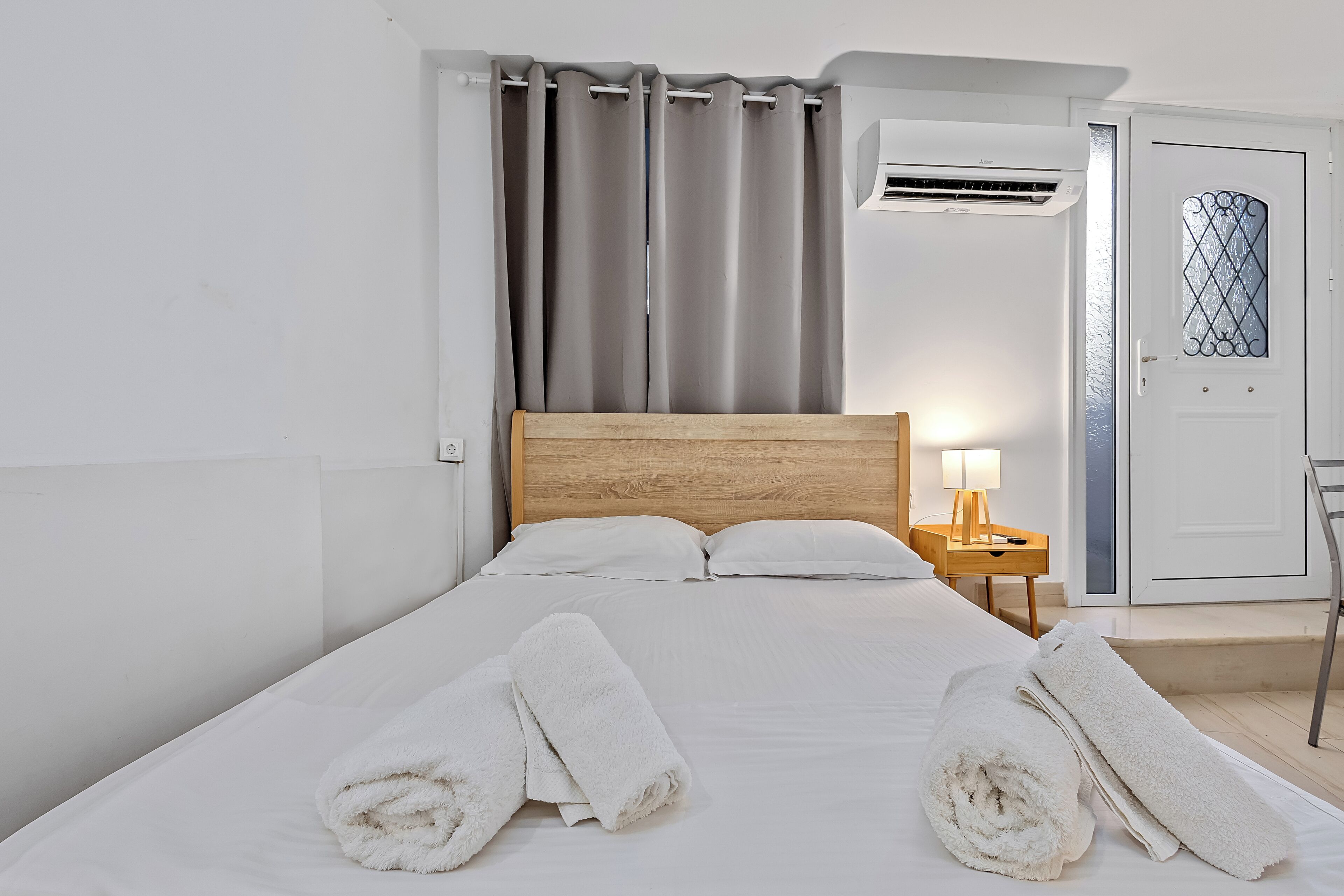 A hotel room with a bed, a nightstand with a lamp, a wardrobe, and a window with curtains.