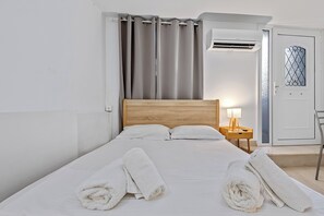 A hotel room with a bed, a nightstand with a lamp, a wardrobe, and a window with curtains. - Athens Plaka Family Suites (Athens)