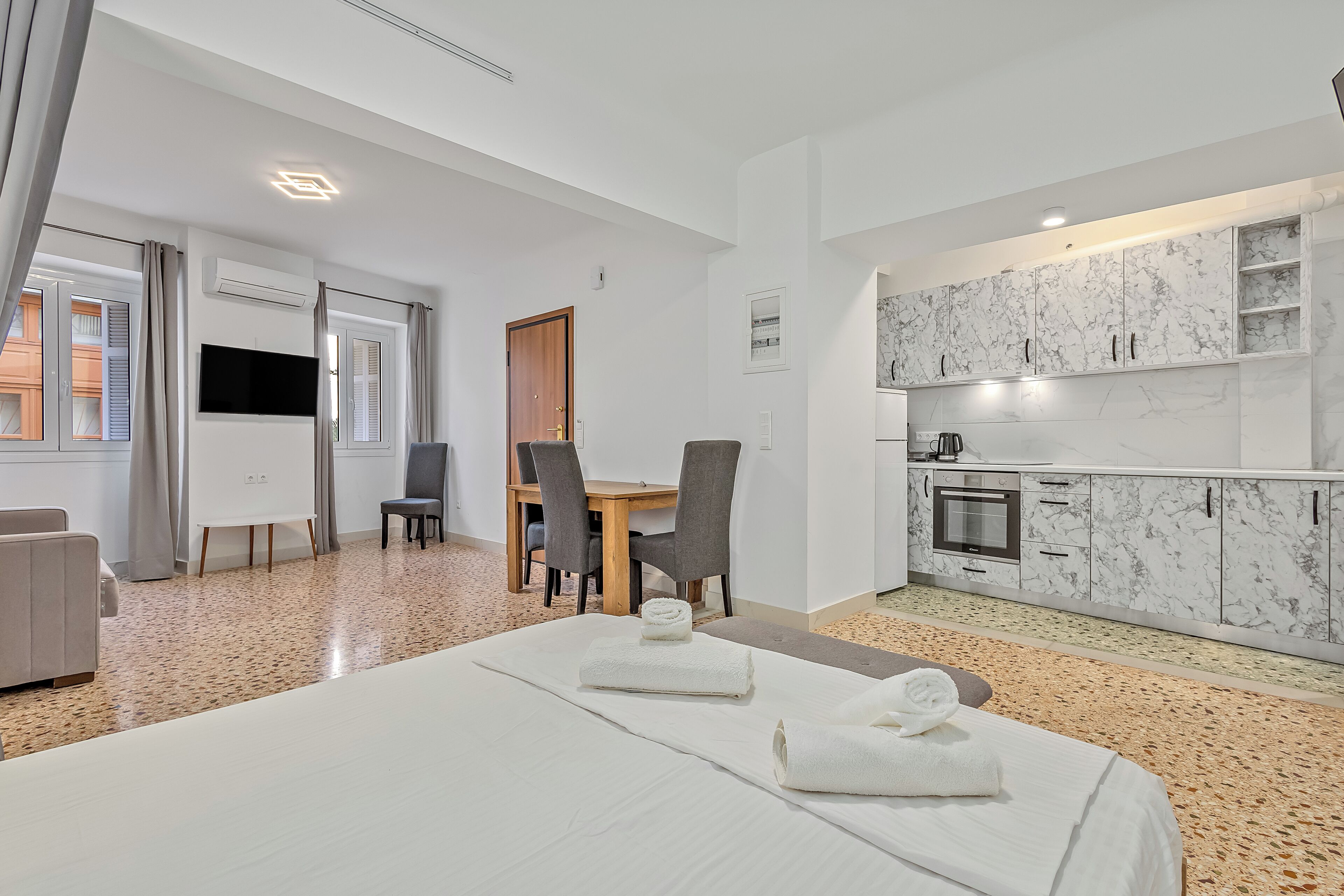 Une chambre d’hôtel comprenant un lit, une table à manger avec des chaises, un coin cuisine avec des placards en marbre et un téléviseur.