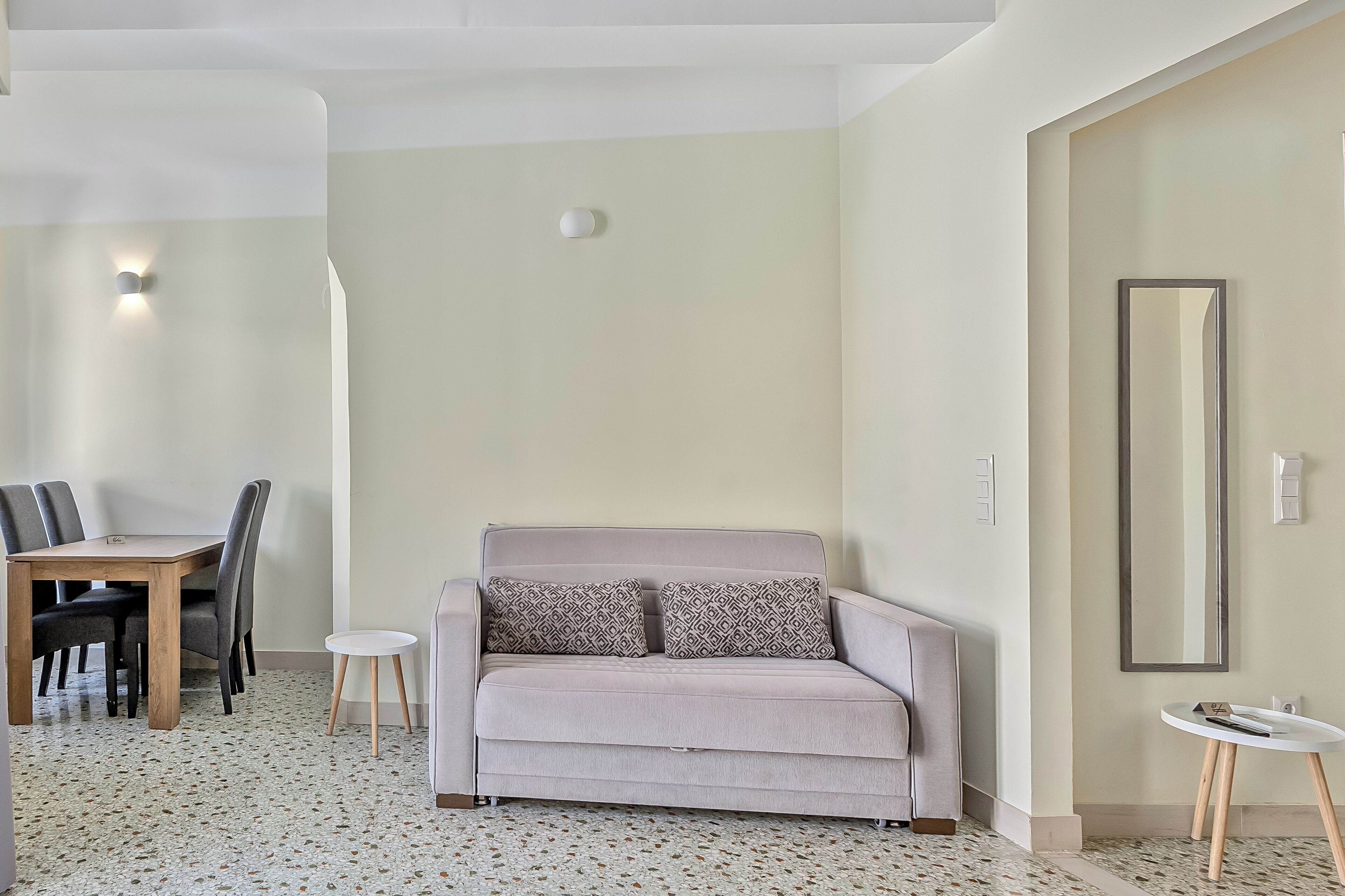 Een woonkamer met een bank, een eettafel met stoelen, een kleine ronde tafel en een spiegel aan de muur.