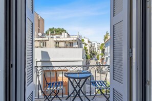 A balcony with a table and two chairs, overlooking a street with buildings and a clear sky. - Athens Plaka Family Suites (Athens)