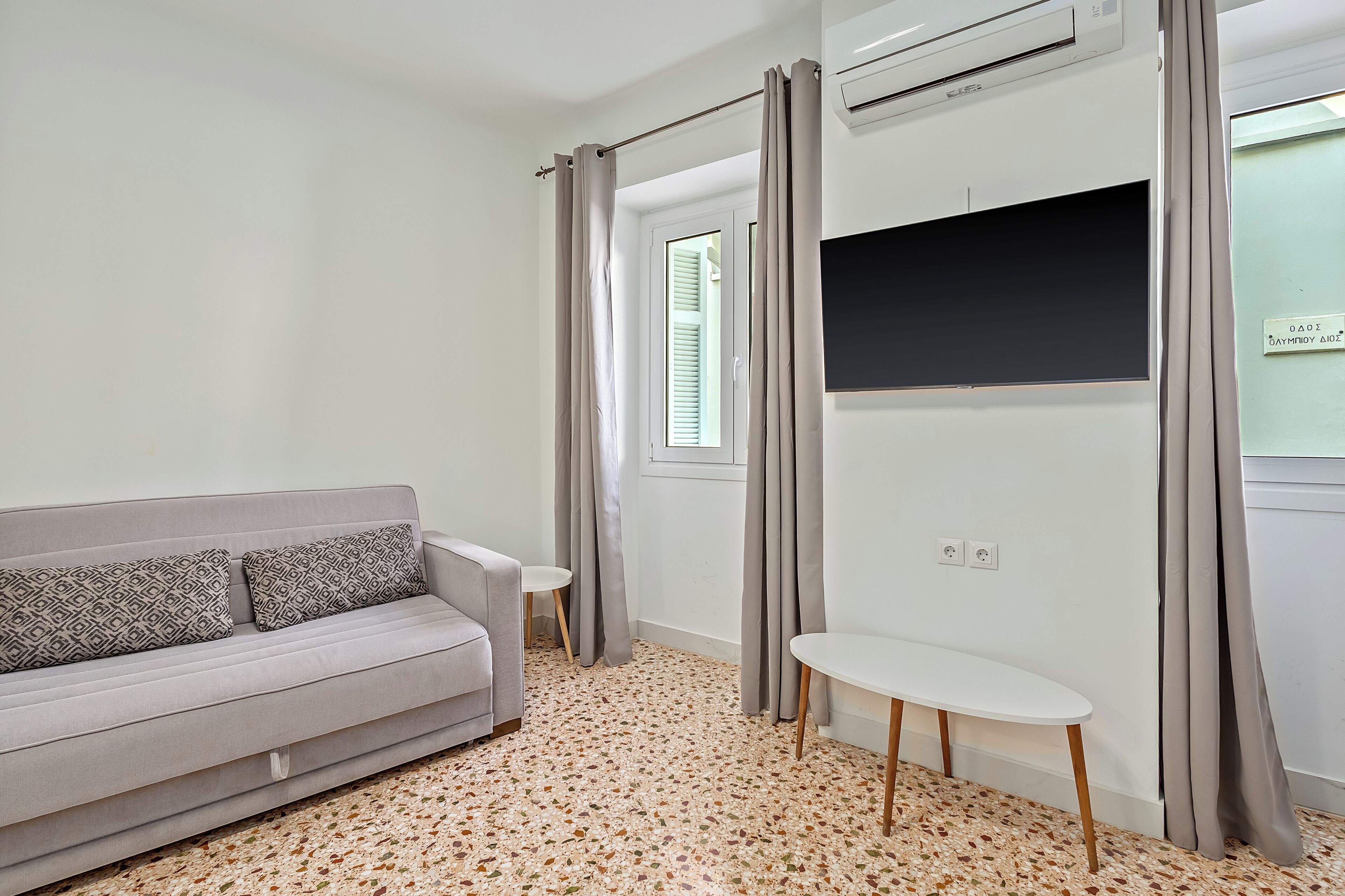 A modern living room with a grey sofa, a small white table, and a wall-mounted TV.