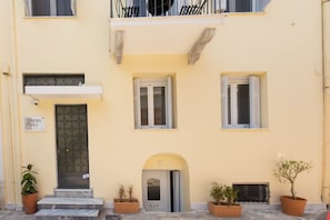 A building with a yellow facade, a door with a glass panel, and two windows with shutters. - Athens Plaka Family Suites (Athens)