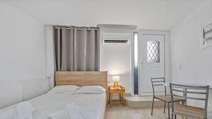 A bedroom with a bed, a bedside table with a lamp, a chair, and a door with a window. - Athens Plaka Family Suites (Athens)