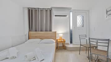 Un dormitorio con una cama, una mesita de noche con lámpara, una silla y una puerta con ventanal.