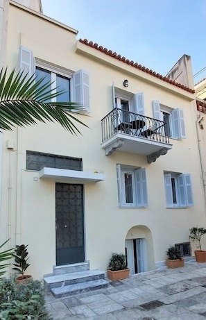 A two-story building with a balcony, a door with a glass panel, and potted plants. - Athens Plaka Family Suites (Athens)