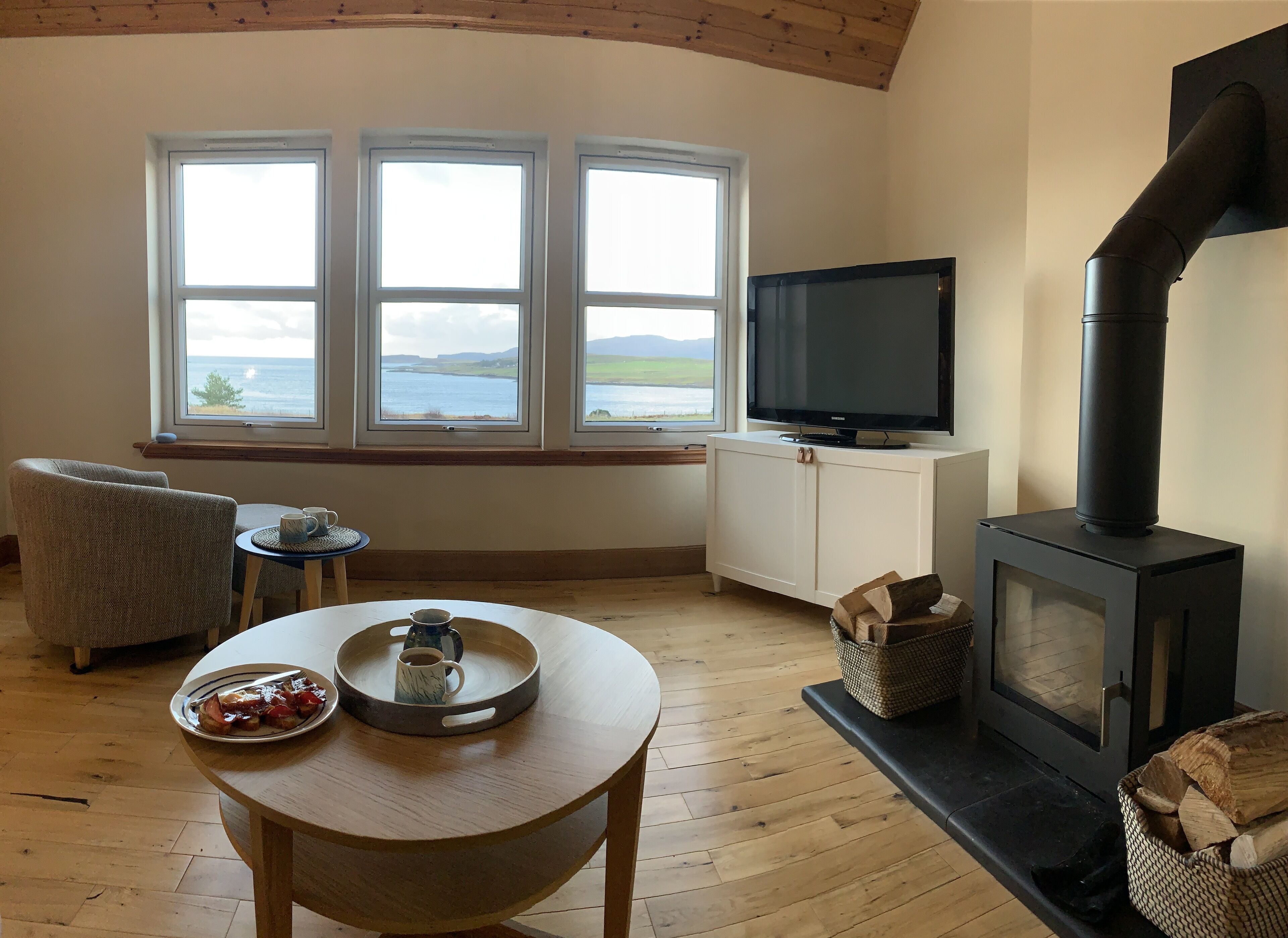 A cozy living room with a large window, a television, a fireplace, and a dining table with a tray.