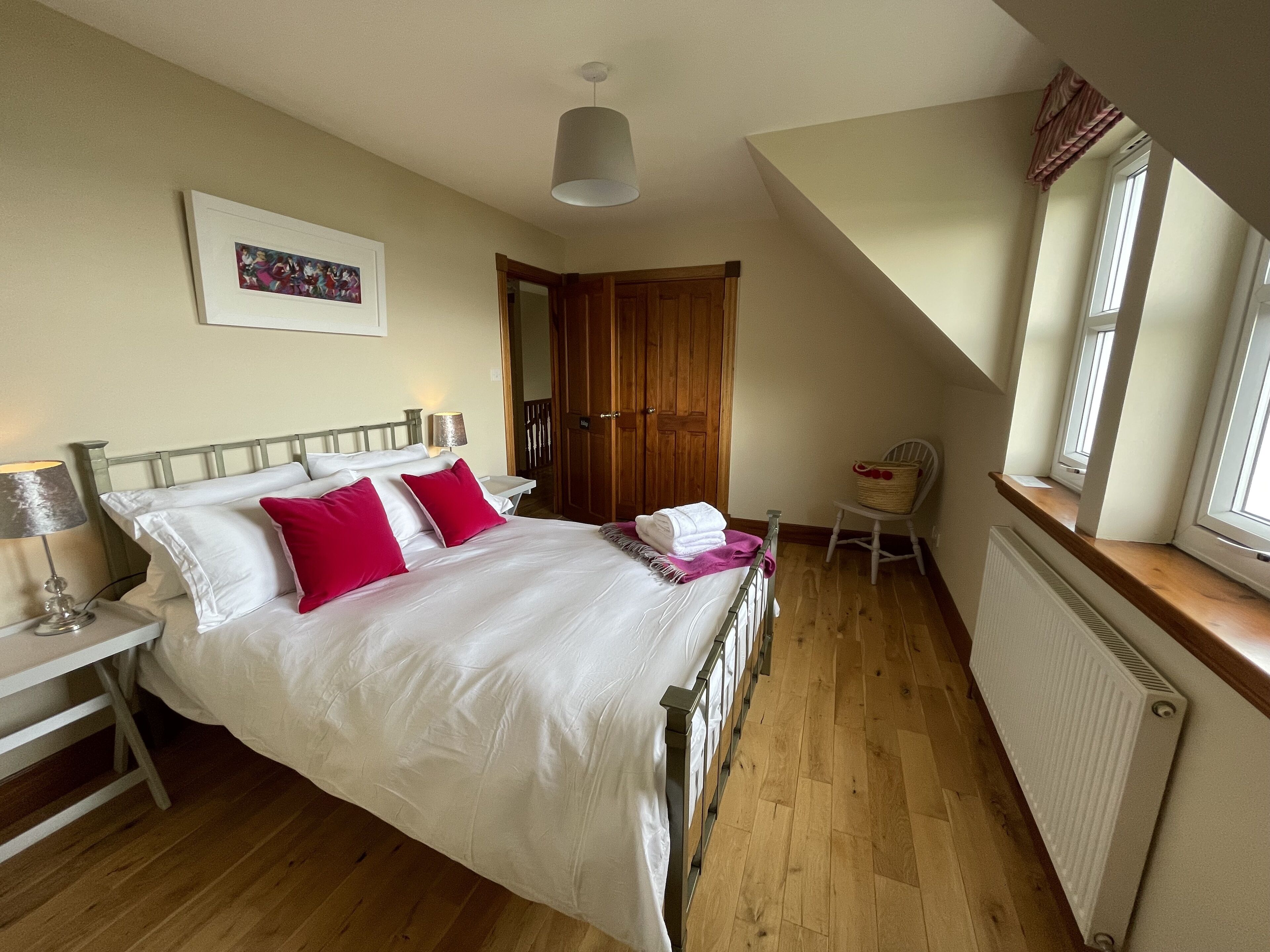 A bedroom with a bed, a nightstand, a lamp, a chair, a window, and a radiator.