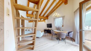 A modern living room with a wooden ceiling, a chandelier, a TV, and a dining area with chairs and a table.