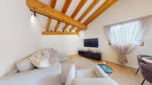 Un salon moderne avec un plafond haut, un téléviseur à écran plat, un ensemble de canapés, une table basse et un coin repas.