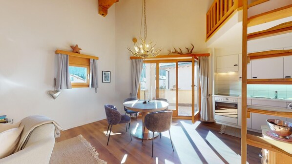 A modern living room with a round table, two chairs, a sofa, and a kitchen area with a sink and stove.