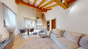 A spacious living area with a high ceiling, a dining table with chairs, a sofa, and a staircase leading to an upper level. - Beautiful, stylishly furnished 2-room flat on the 2nd floor with gallery, 60 m2, (Sils/Segl Maria)