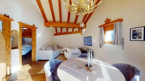 A cozy room with a wooden ceiling, a white sofa, a dining table with chairs, and a TV on the wall.