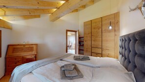 A bedroom with a wooden ceiling, a bed with white bedding and grey towels, a wooden dresser, and a wardrobe with a mirror.