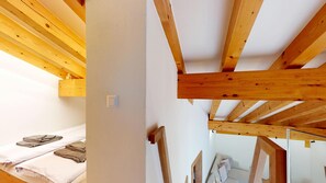A room with a wooden ceiling structure, a bed with towels, and a white wall. - Beautiful, stylishly furnished 2-room flat on the 2nd floor with gallery, 60 m2, (Sils/Segl Maria)