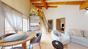 A modern living room with a dining area, a staircase, and a kitchen.