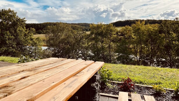Une terrasse en bois donnant sur un champ verdoyant, avec des arbres et une colline au loin.
