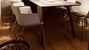 Une salle de conférence avec une longue table, des chaises blanches, un luminaire suspendu et des rideaux gris.
