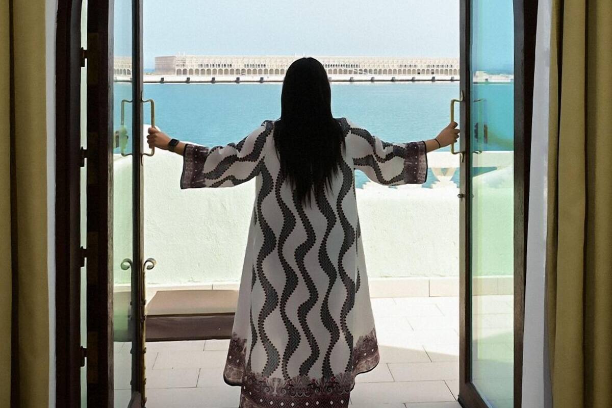 A person standing at a doorway with arms outstretched, overlooking a waterfront with a bridge and buildings.