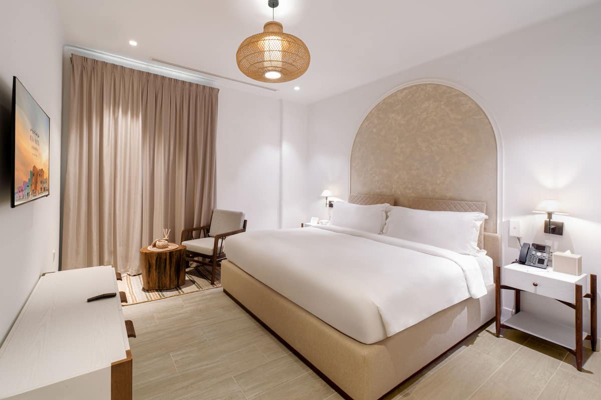 A hotel room with a large bed, a desk, a chair, a round table, and a wall-mounted TV.
