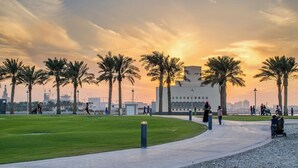 A park with palm trees, a pathway, and a building in the background. - Mina Hotel and Residences By the Torch (Doha)