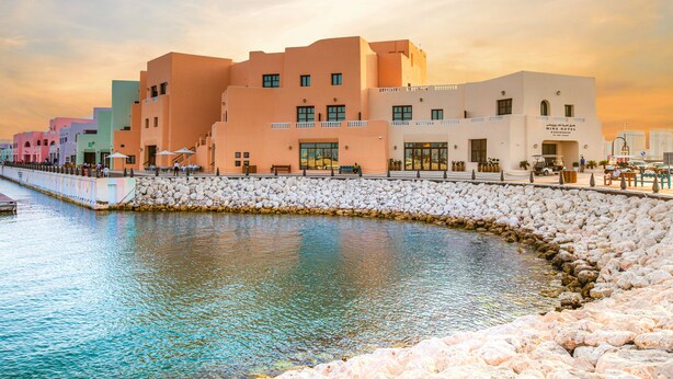 A waterfront hotel with multiple buildings, a stone wall, and a calm water body. - Mina Hotel and Residences By the Torch (Doha)