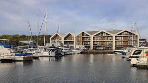 A marina with several boats docked and a modern building with multiple balconies and large windows.
