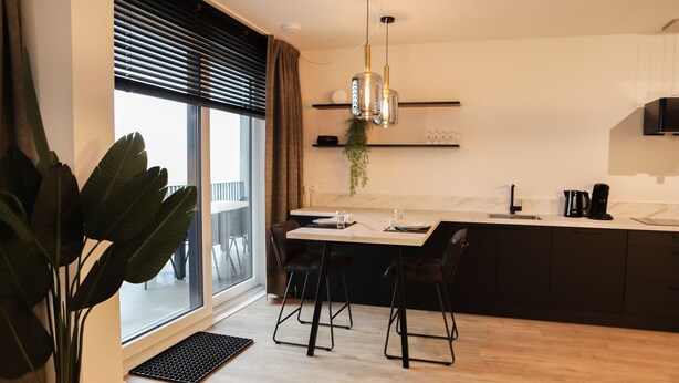 A modern kitchen with a large window, a dining area with two chairs, a coffee maker, and a hanging light fixture.