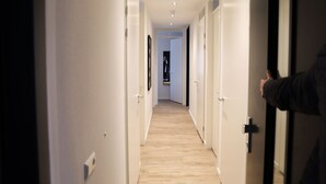 A hallway with doors on both sides, leading to a room with a wooden floor and a visible door at the end.