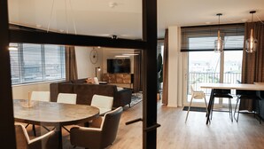 A modern living room with a round dining table, comfortable seating, a TV, and a balcony with a view.