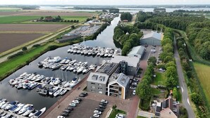 An aerial view of a marina with numerous boats docked, a large building with a sloped roof, and a road running alongside.