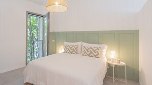 A bedroom with a bed, a bedside table with a lamp, and a window with a view of trees. - Salvia Ginepro Apartments (Como)