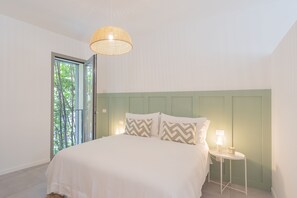 Une chambre à coucher avec un lit, une table de chevet avec une lampe et une fenêtre donnant sur des arbres.