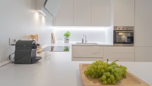 A modern kitchen with a built-in oven, a coffee machine, and a wooden cutting board with grapes. - Salvia Ginepro Apartments (Como)